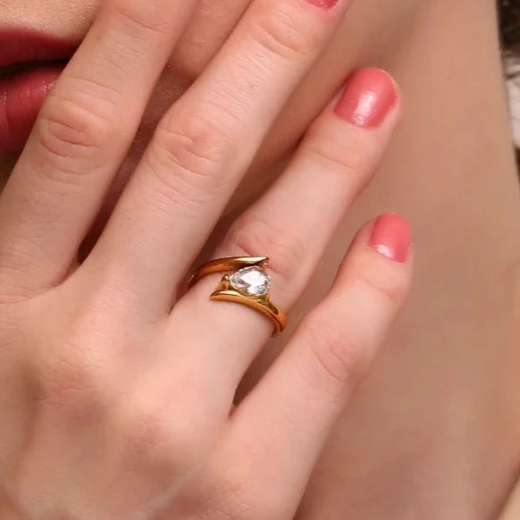 Close-up of a hand wearing a gold ring with a diamond, against a neutral background.